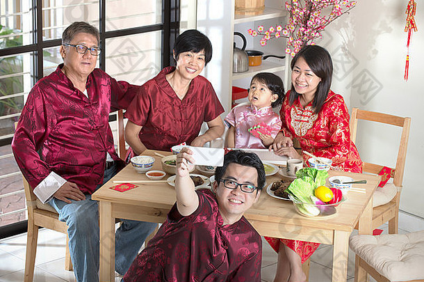 庆祝中国新年，吃团圆饭。快乐亚洲华人多代同堂用餐时身着红色旗袍自拍