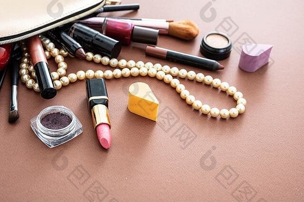 用专业配件制作化妆包。唇膏和刷子从棕色背景下的金色化妆包中取出，空间。
