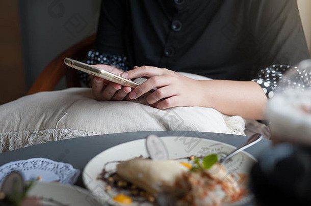 周末，一位女士在咖啡馆用智能手机进行社交媒体。咖啡馆的度假生活