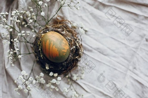 木<strong>制</strong>桌子上乡村巢穴中的<strong>时尚</strong>复活节彩蛋。<strong>天然</strong>染色的绿色复活节彩蛋，带有白色的春花，以乡村纺织品为背景。特克斯空间