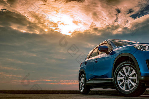 傍晚日落时，蓝色紧凑型SUV轿车停在海边的水泥路上，具有运动和现代设计。混合动力和电动汽车技术
