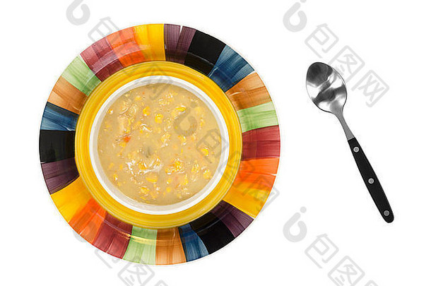 一碗老式浓浓的奶油玉米杂烩的俯视图，在一个彩色的盘子上，碗的侧面有一个汤匙