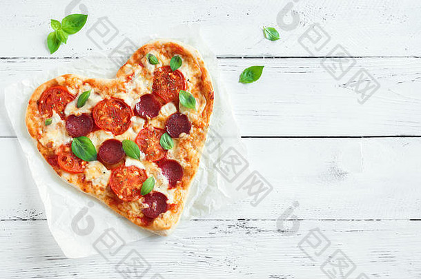 木质背景上的心形比萨饼，带有空间。情人节用番茄、意大利香肠、意大利干酪和罗勒做成的比萨饼。