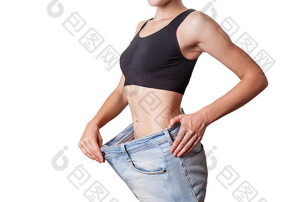穿着大牛仔裤的年轻女子纤细腰围的特写镜头，展示了成功减肥、白色背景上的孤立、饮食观念。