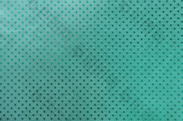 深色绿松石色背景，金属箔纸上有闪闪发光的星星图案特写。青色金属化包装假日纸表面纹理。