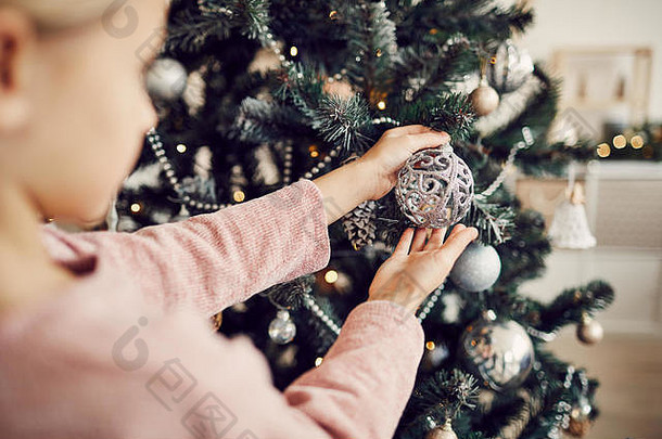 特写镜头：小女孩手里拿着美丽的球体，看着圣诞树上的球体
