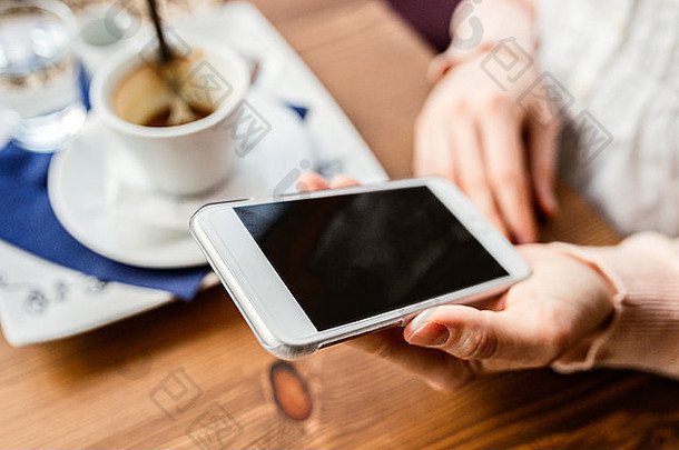 在咖啡馆喝咖啡的一个拿着智能手机的不可辨认的女人