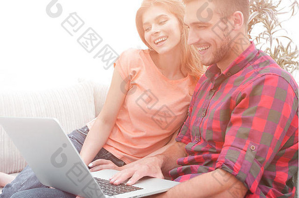 坐在沙发上带着笔记本电脑微笑的年轻夫妇