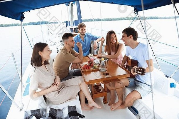 一群快乐的朋友在户外的船上聚会上喝着<strong>伏</strong>特加鸡尾酒，兴高采烈。年轻人在海上玩吉他旅游，有青春和<strong>暑</strong>假的概念。喝酒、度假、休息。