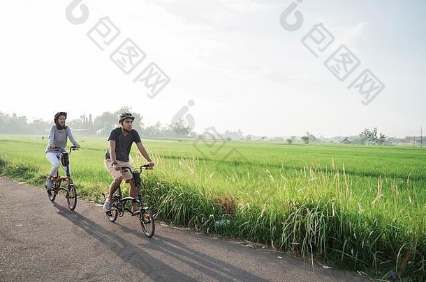 年轻的夫妇穿头盔骑<strong>折叠自行车</strong>大米字段背景