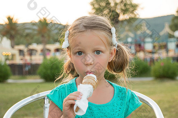 可爱的金发小女孩穿着绿色t恤，在<strong>夏日</strong>阳光下吃着<strong>冰淇淋</strong>。暑假，甜点概念。大眼睛的可爱孩子吃白色<strong>冰淇淋</strong>。
