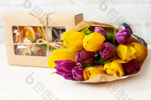 新鲜花束紫黄色郁金香，<strong>牛皮纸包装</strong>，一盒手工制作的糖果。糖果和鲜花，给他爱的女人的礼物