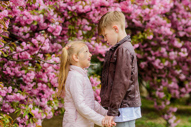 恋爱中的孩子粉色樱花。爱在空气中。一对可爱的孩子漫步樱花花园。温柔的爱情。小女孩和男孩。在公园里的浪漫约会。春天是坠入爱河的时候。