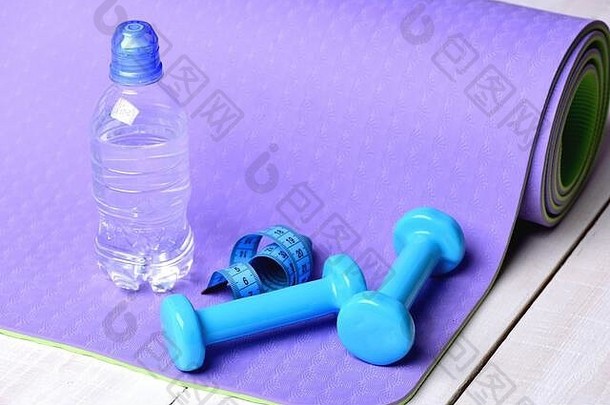 塑造健身设备锻炼体育运动概念杠铃水瓶青色测量磁带卷说谎紫色的瑜伽席哑铃使蓝色的塑料光木背景