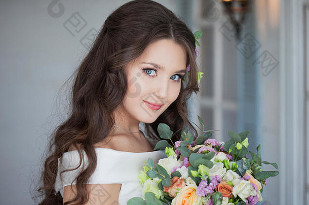 一位年轻美丽的新娘子的肖像，穿着白色连衣裙，带着一束美丽蓬松的鲜花。