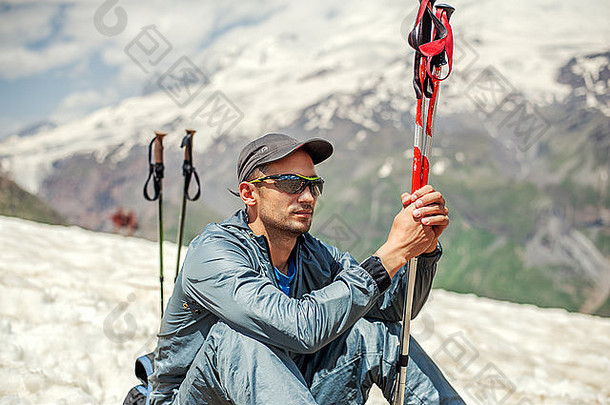 年轻的登山者坐在雪山上，靠近雪盖山顶，手持登山杖。厄尔布鲁克山背景