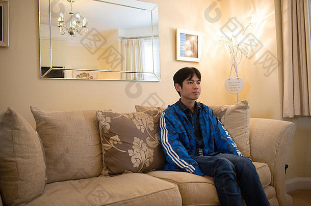 一名海外亚洲<strong>留学</strong>生坐在学生公寓起居室的沙发上看电视。