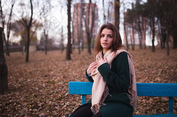 美丽的年轻的浅黑肤色的女人女人坐着板凳上秋天公园
