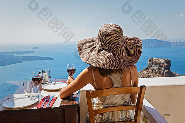 戴帽子的年轻女子喝着红酒看着美丽的大海