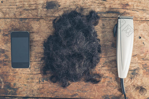 一部智能手机，一堆头发和一些理发器放在一张木桌上