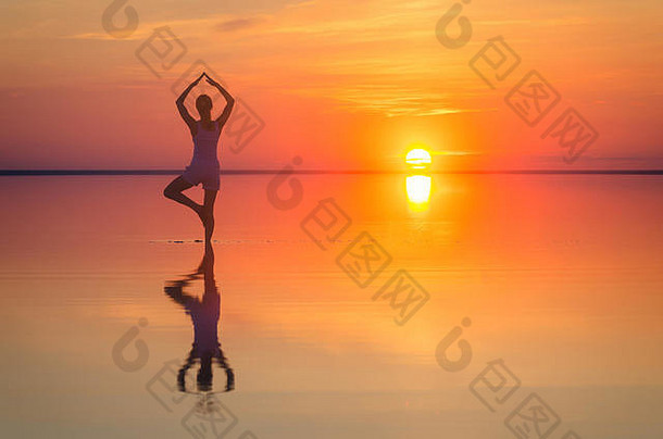 美丽的女模特在海边夕阳下张开双臂。盐湖埃尔顿平静的海水折射出女人的轮廓。太阳落在地平线后面。那个女孩独自一人