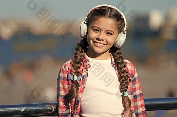 孩子们用现代耳机在户外听音乐。小女孩戴着耳机听歌曲。音乐帐户播放列表。定制您的音乐。城市儿童休闲。小孩子放松。音乐无处不在。
