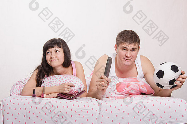 一个年轻的女孩和一个躺在床上的男人。漂亮的女孩修指甲，男人在电视上看足球。
