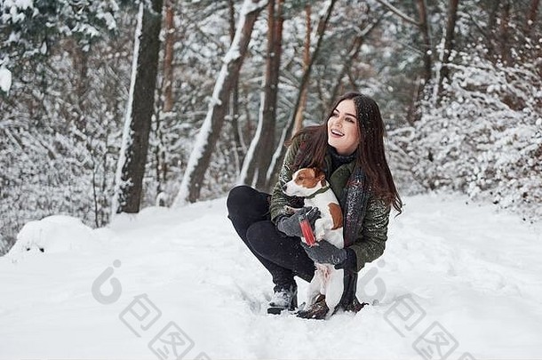 我们应该<strong>去哪</strong>里。带着微笑的黑发女郎和她的狗在冬季公园散步时<strong>玩</strong>得很开心