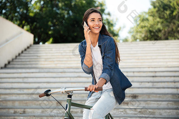 一个年轻开朗的女孩骑着<strong>自行车</strong>，一边用手机聊天，一边往户外看