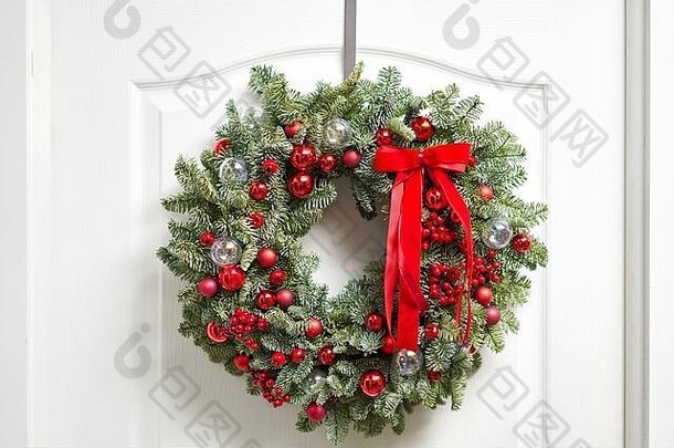 白色的门上挂着美丽的红色圣诞花环，上面缀着新鲜的云杉。<strong>房子</strong>的入口。圣诞节的气氛。圣诞树。