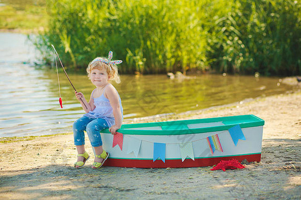 一个穿着红色泳衣的可爱小女孩站在海滩上，船的背景衬托着她。