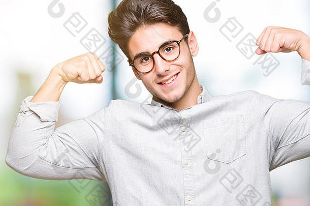 年轻英俊的男子戴着眼镜，在孤立的背景下露出手臂肌肉，自豪地微笑着。健身理念。