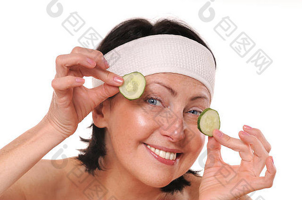 快乐成熟的女人，眼睛前拿着黄瓜片。天然水疗。在白色背景上隔离
