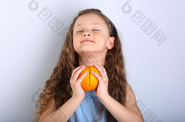 可爱的微笑快乐孩子女孩卷曲的头发风格持有手柑橘类橙色水果片打开享受眼睛蓝色的背景