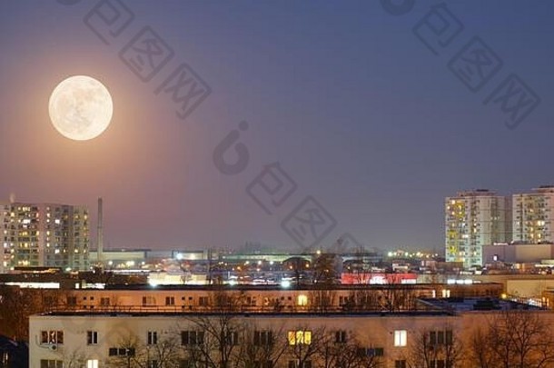 满月在蓝色的时刻出现在城市景观上。空间。
