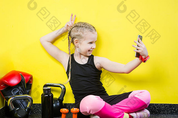 年轻的高加索人女孩孩子使照片坐着地板上内部健身房女运动员持有电话发送照片视频