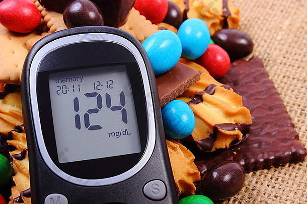 血糖仪上有成堆<strong>的</strong>糖果和饼干放在黄麻麻布上，太多<strong>的</strong>糖果，<strong>糖尿病的</strong>概念