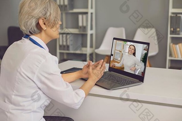 高级医生在医院与年轻患者视频聊天。医生在她的办公室用笔记本电脑与客户交谈