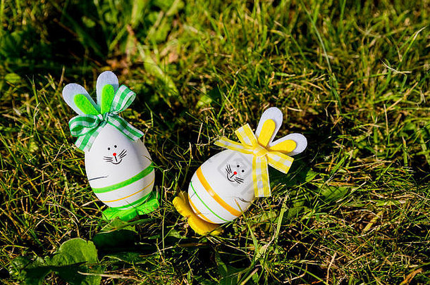 以绿色草地为背景，以复活节彩蛋为复活节兔子的可<strong>爱创意</strong>照片。复活节快乐贺卡。兔子复活节彩蛋。复活节假期概念与两个可爱的手工鸡蛋：兔子