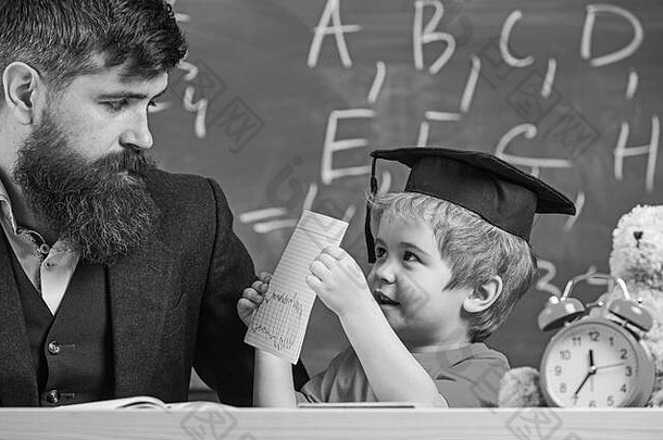 老师父亲检查家庭作业帮助男孩儿子个人研究概念老师正式的穿学生学位帽教室黑板背景忙孩子研究学校