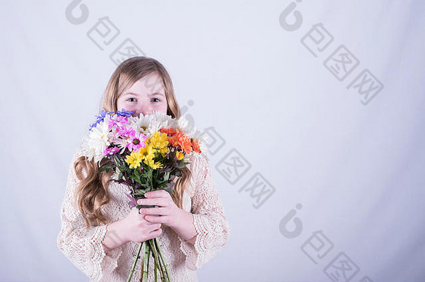 一个12岁的女孩，留着一头又长又脏的金发，她的下半脸上挂着一束五颜六色的雏菊，在白色背景下，她微笑着睁开眼睛