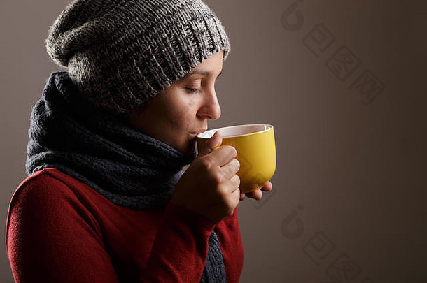 戴着羊毛围巾和帽子喝热茶的年轻女子。秋冬季节与疾病概念。