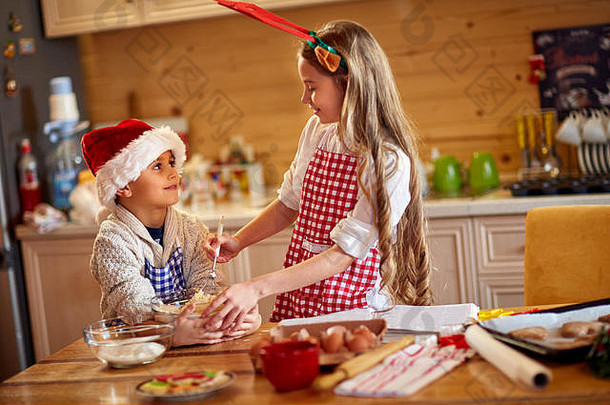 两个戴着圣诞帽的可爱孩子，在家里准备圣诞饼干
