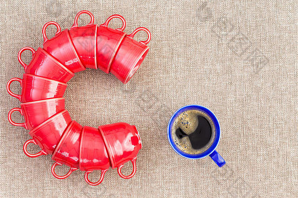 十一个红色的杯子，以字母C的形式堆放在一个装满咖啡的蓝色杯子旁边，这是关于摩尼时代第一件事的概念