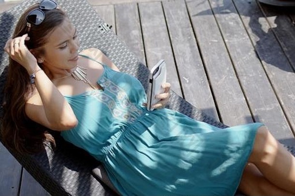 穿着蓝色连衣裙的女士在休息室的椅子上休息，并使用智能手机