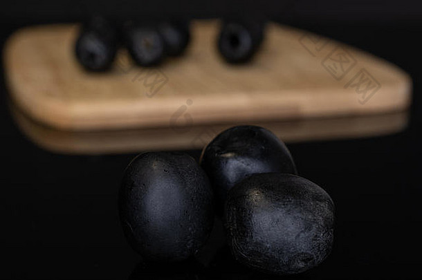 八人一组，整个美味的黑橄榄放在竹砧板上，在黑色玻璃上隔离