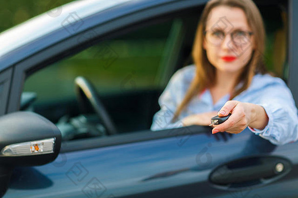 年轻漂亮的女士坐在车里，手里拿着钥匙——购买二手车或租车的概念
