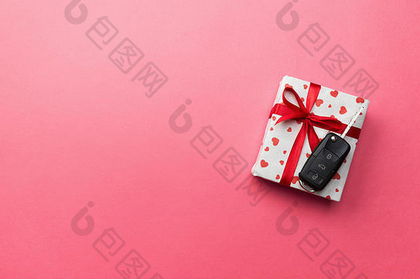 带红色丝带蝴蝶结的纸质礼品盒上的车钥匙和粉红色桌子背景上的心形钥匙。假日呈现顶视图概念。