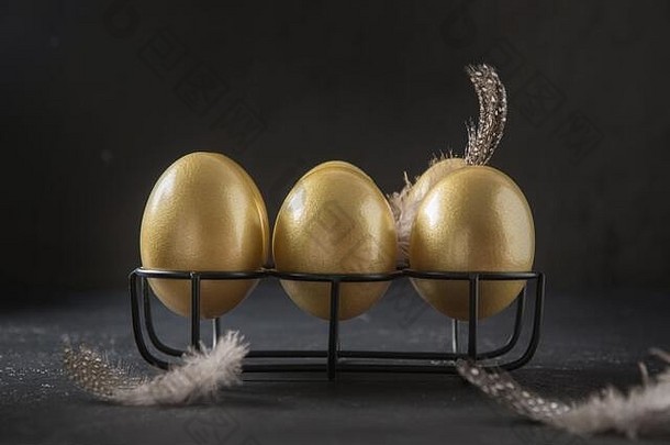 站在黑色背景上装饰羽毛的金鸡蛋。复活节黑暗概念。闭合。