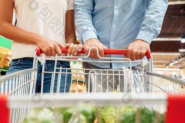 日常购物。在超市里，一对夫妇提着装满蔬菜的手推车走在一起